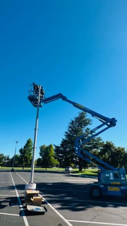 Aerial lift platform extended upward with worker maintaining street light pole on clear sunny day