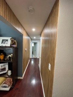 Modern hallway with wood paneling, recessed lighting, and dark flooring