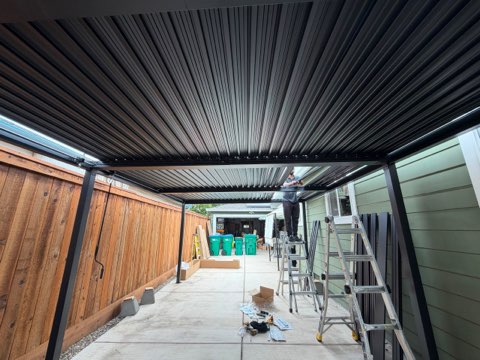 Metal corrugated pergola covering residential driveway with wooden gates and ladder