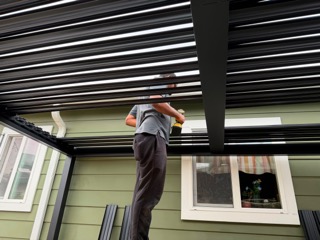 Worker installing light fixture on exterior wall of green house