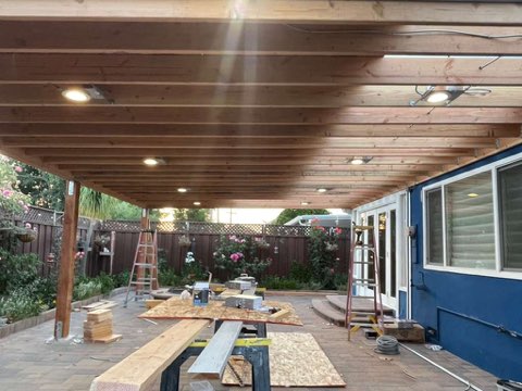 Covered patio with wooden ceiling, construction materials, and blue house exterior during renovation