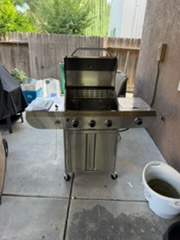Stainless steel gas grill on patio with black cooking hood and side burner