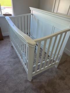 White wooden baby crib with spindle sides on carpet in bright room