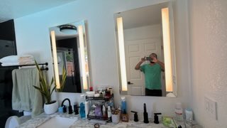 Bathroom vanity with illuminated mirror, sink, toiletries, and towel rack