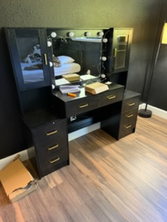 Black vanity desk with lighted mirror, drawers, and organized makeup and beauty products