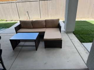Modern patio furniture set with gray sectional sofa, black coffee table, and ottoman on concrete patio