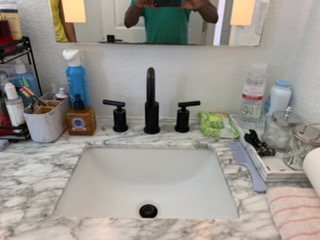 Bathroom sink with marble countertop, black faucet, and various toiletries and products