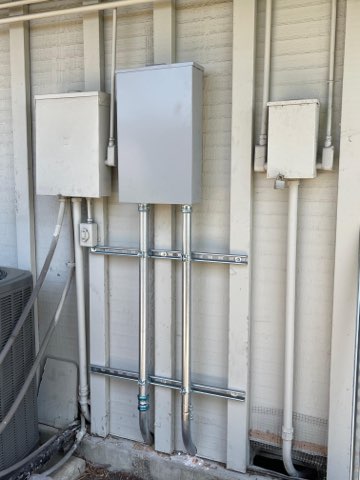 Outdoor electrical panel mounted on brick wall with conduit piping and disconnect switches