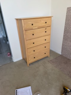 Light wood five-drawer chest with black knobs in bedroom setting
