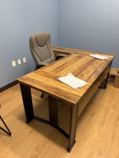 Modern wooden desk with black metal base and gray upholstered chair in office space