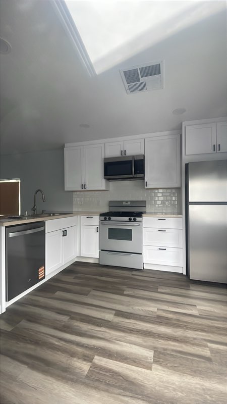 Modern kitchen with white cabinetry, stainless steel appliances, and wood-look flooring
