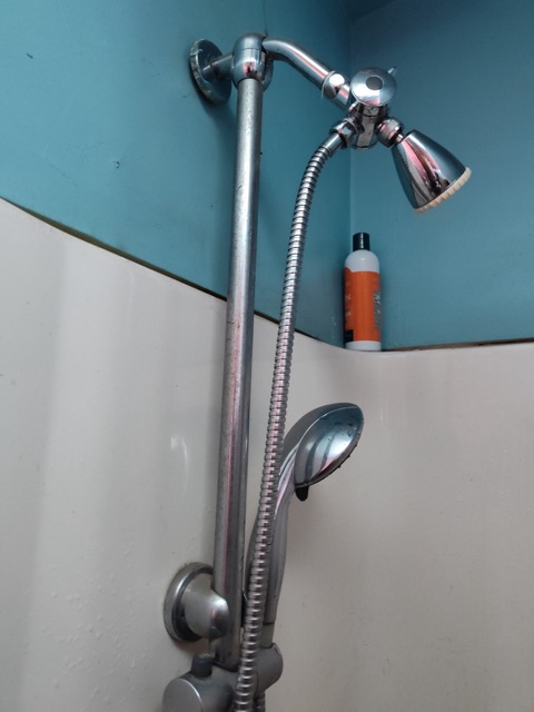 Chrome shower fixture with dual showerheads and handheld sprayer on tiled bathroom wall