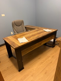 Modern office desk with wooden top and black metal frame, tan leather chair, gray walls