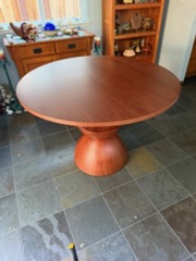 Round wooden pedestal dining table in cherry finish on slate floor