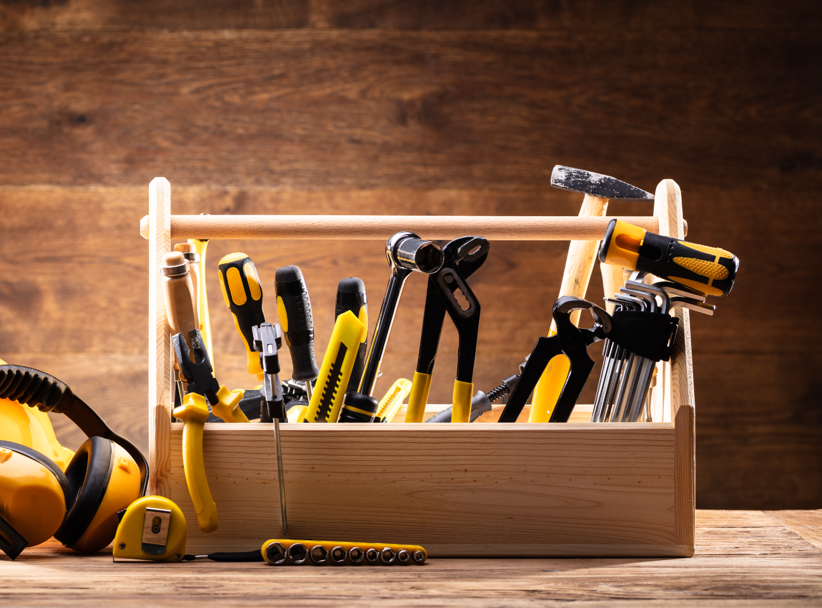 Wooden toolbox filled with yellow and black hand tools on wooden surface