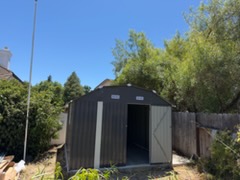 Black prefabricated shed with open door in hillside garden setting